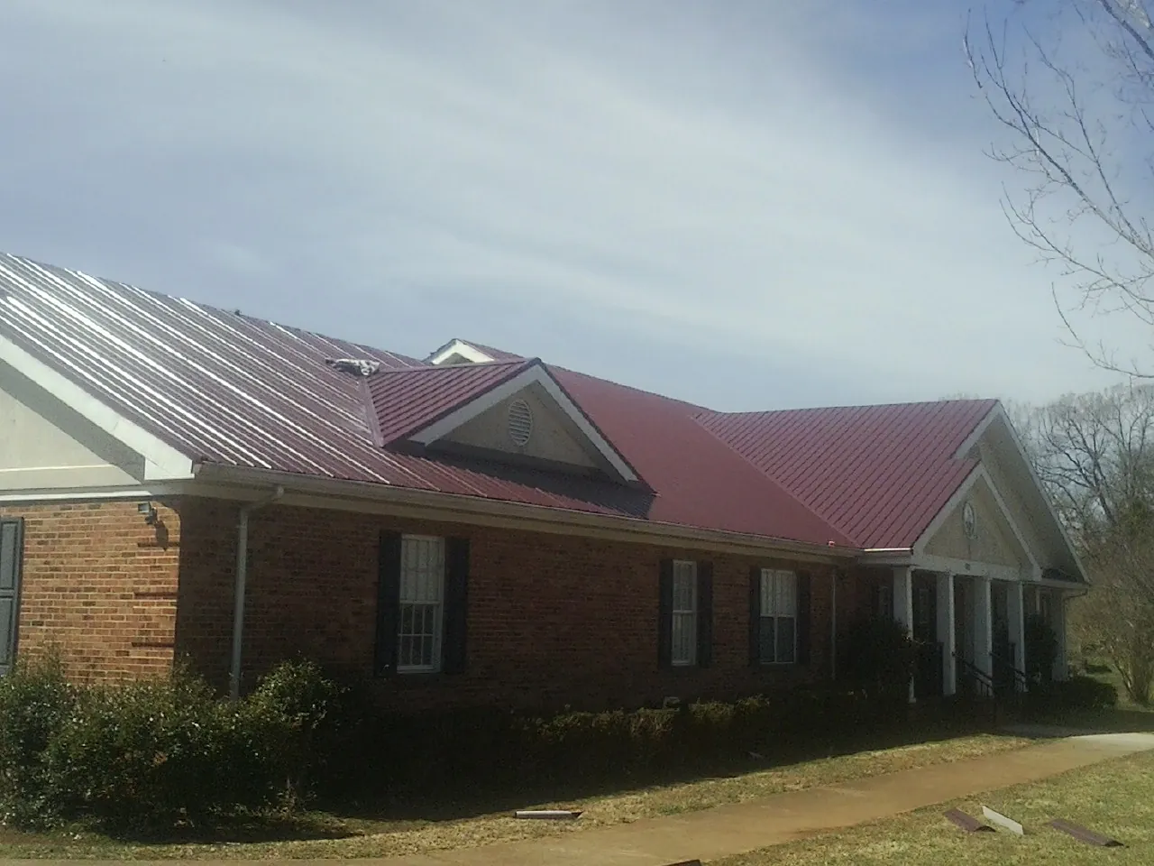 Red metal roof with gabled entries on a long brick building, from a Hail Damage Roof Repair job in Marblemount