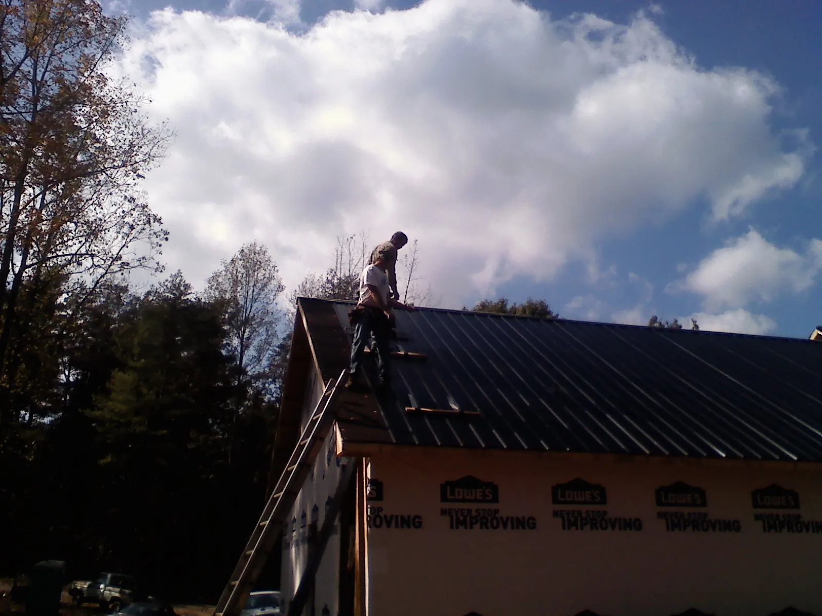 Roofer fastening dark metal panels high against a cloudy sky, from a Roof Inspection job in Marblemount
