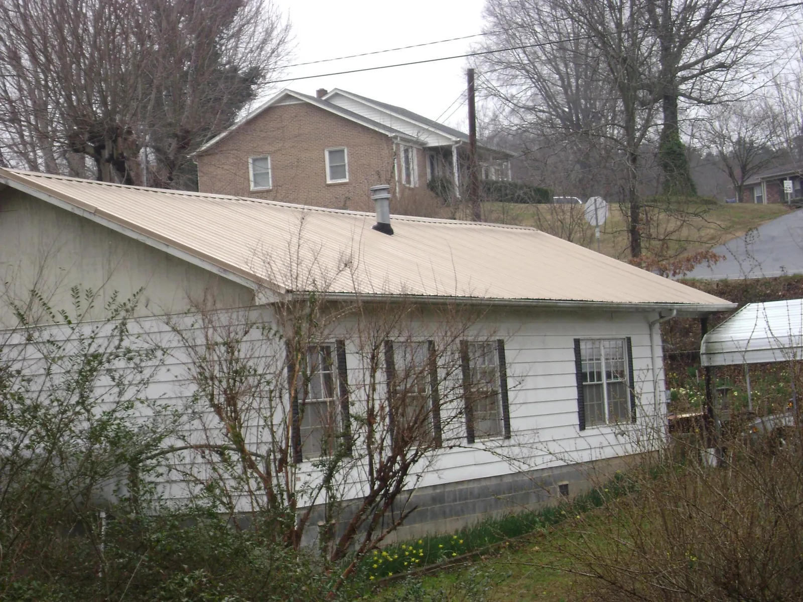 Tan metal roof on a white sided house set into a hillside — Commercial Roofing by Roofing Brothers in Marblemount